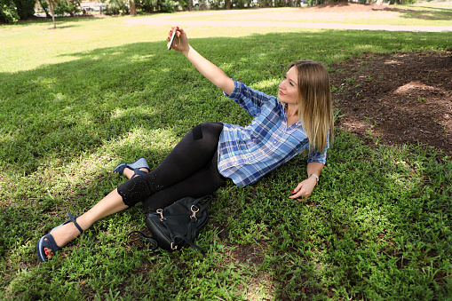 Outdoor portrait of beautiful young adult caucasian woman with smart phone in public park