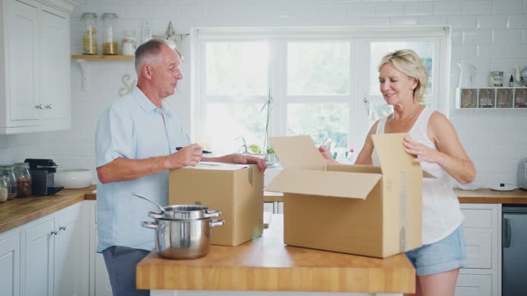 Senior Couple Downsizing In Retirement Packing And Labelling Boxes Ready For Move Into New Home