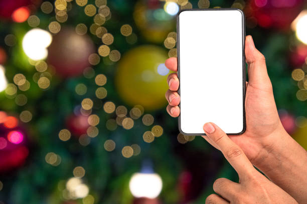 istock Close up hand holding phone isolated on white background with Illuminated  blurred bokeh of  Christmas tree decoration with  hanging lights ball. 1290195072
