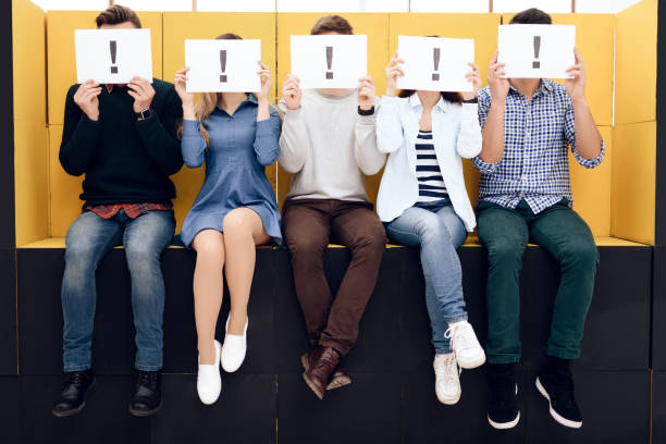 istock Group of people holding exclamation mark sign, sitting on black boxes. 1290213794