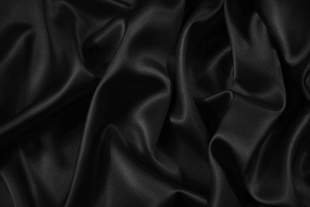 istock Black silk satin fabric background. Black elegant background. Dark liquid wave or black silk with wavy folds. 1290215348