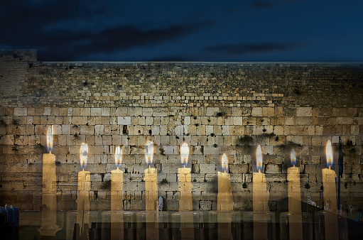 Digital composite image of menorah with glittering candles and western wall in Jerusalem. Image symbolizes Hanukkah Holiday and Jewish desires and hopes. Low key image toned for retro style, focus on wall and candles