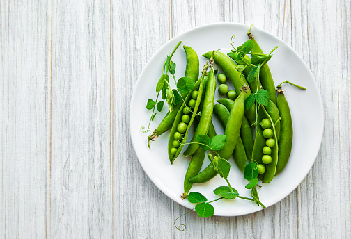 Green peas in a plate on a white wooden  background. View from above.