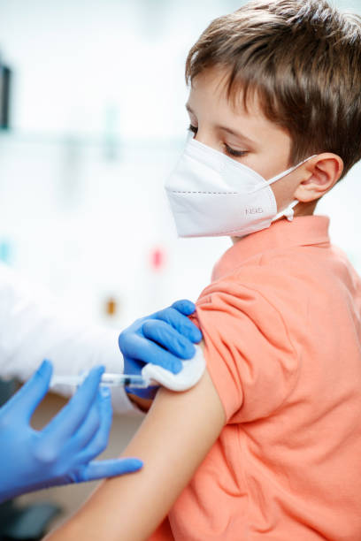 istock Boy wearing protective face mask looking at doctor's hand injecting vaccine into his arm 1290219544