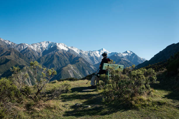 A backpacker sitting on the bench and admiring the snow-capped mountain peaks from Mt Fyffe track, South Island, New Zealand
