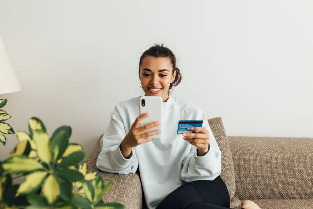 mujer sonriente usando el teléfono inteligente y la tarjeta de crédito. mujer joven haciendo una compra en línea. - ecommerce fotografías e imágenes de stock