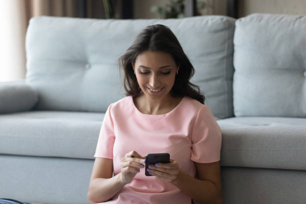 istock Smiling millennial multiracial woman using smartphones, sitting on floor. 1290228404