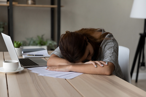 Exhausted unmotivated young female worker fallen asleep at table working with paper documents, feeling lack of energy at workplace, sleepy woman tired of exam preparing or studying at home office.