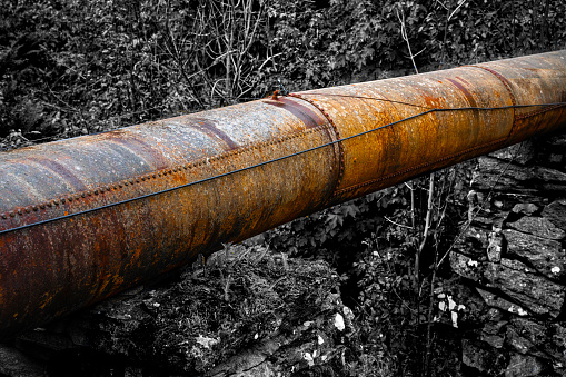 Large rusted and old industrial pipeline running through rough nature.