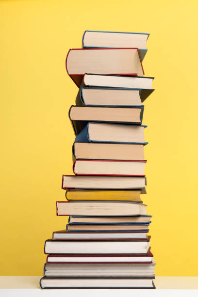 istock Pile of books stacked on a yellow background with space for copy in a vertical image 1290234806