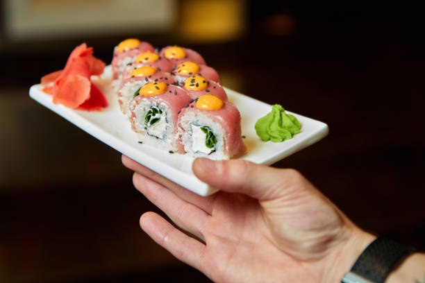 istock Waiter holding a set of sushi rolls on a white plate. Close-up, selective focus 1290235665