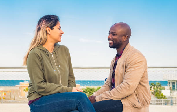 istock young interracial couple sitting at seaside on a bench looking at each other and interactig.happy people outside on autumn holidays.fiends on leasure time and social activities outdoor.relax lifestyle 1290238787
