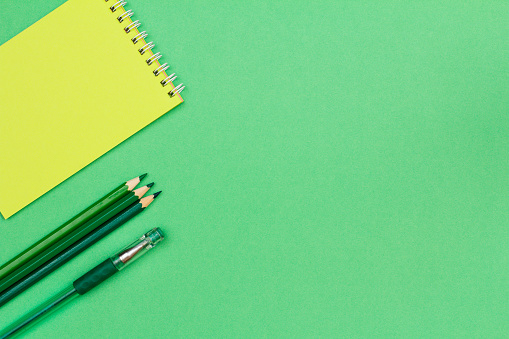 Notebook, color pencils and pen on green background. Top view with copy space. Back to school concept. School supplies.