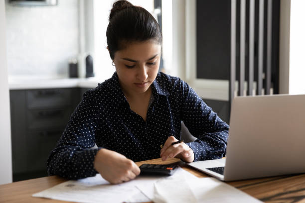 istock Concentrated young indian lady engaged in paperwork using computer calculator 1290242627
