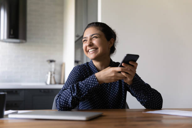 Overjoyed young indian woman holding cellphone laughing on internet joke Cute thing! Excited young indian woman sit at desk hold cellphone look aside celebrate winning online game. Overjoyed hindu lady distracted from phone screen laughing on popular joke internet meme i see you meme stock pictures, royalty-free photos & images
