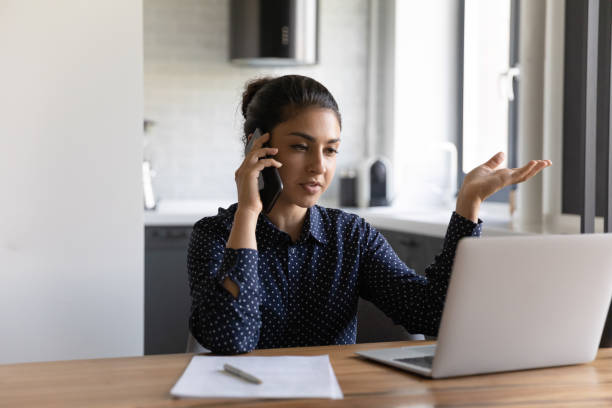 istock Millennial hindu female talking on phone looking at computer screen 1290242662