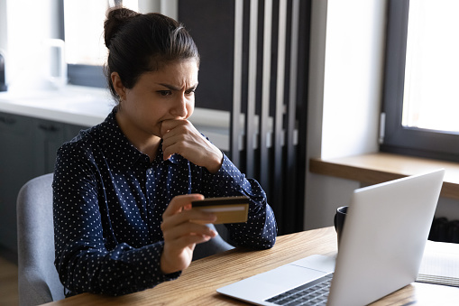 Spend too much. Shocked upset young hindu female shopper check balance of credit card using laptop seeing huge debt. Frustrated indian lady losing money after paying online. Internet scam fraud victim