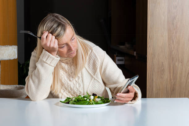 istock middle aged blonde woman  using smartphone while eating salad in the kitchen 1290242887