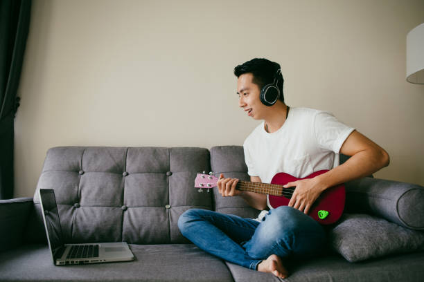istock Young Asian mam having fun playing Ukulele in living room. 1290243014
