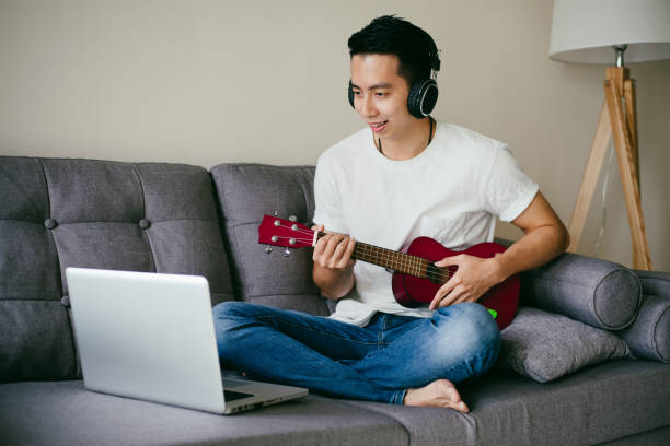 istock Young Asian man having fun playing Ukulele in living room. 1290243216
