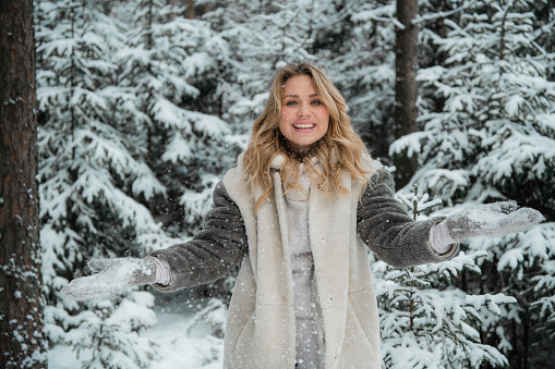 Happy blonde girl with blue eyes throws snow flakes from her hands. Beautiful portrait with bokeh in the winter forest