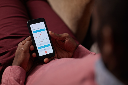 Close-up of African man lying on sofa and using online calendar on his mobile phone he looking at his tasks