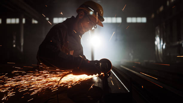 istock Heavy Industry Engineering Factory Interior with Industrial Worker Using Angle Grinder and Cutting a Metal Tube. Contractor in Safety Uniform and Hard Hat Manufacturing Metal Structures. 1290244430