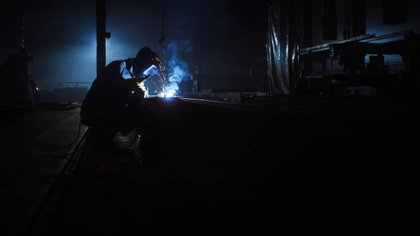 istock Heavy Industry Engineering Factory Interior with Industrial Worker Using a Welding Machine and Working on a Metal Tube. Contractor in Safety Uniform and Hard Hat Manufacturing Metal Structures. 1290244451