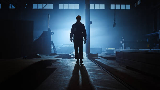 istock Professional Heavy Industry Engineer/Worker Wearing Uniform, Flashlight on the Hard Hat in a Steel Factory. Industrial Specialist Walking Towards the Camera in a Dark Metal Construction Manufacture. 1290244468