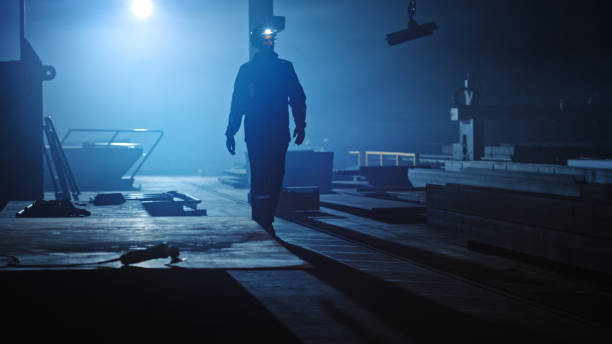 istock Professional Heavy Industry Engineer/Worker Wearing Uniform, Flashlight on the Hard Hat in a Steel Factory. Industrial Specialist Walking Towards the Camera in a Dark Metal Construction Manufacture. 1290244474