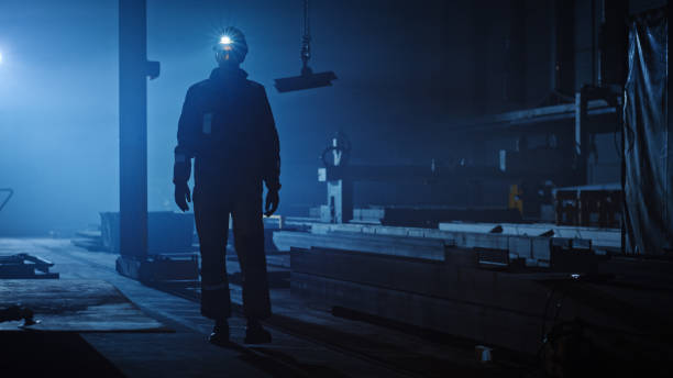 istock Professional Heavy Industry Engineer/Worker Wearing Uniform, Flashlight on the Hard Hat in a Steel Factory. Industrial Specialist Walking Towards the Camera in a Dark Metal Construction Manufacture. 1290244475