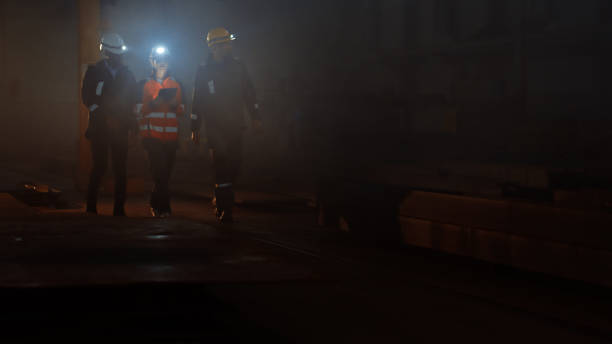 istock Three Diverse Multicultural Heavy Industry Engineers and Workers in Uniform Walk in Dark Steel Factory Using Flashlights on Their Hard Hats. Female Industrial Contractor is Using a Tablet Computer. 1290244531