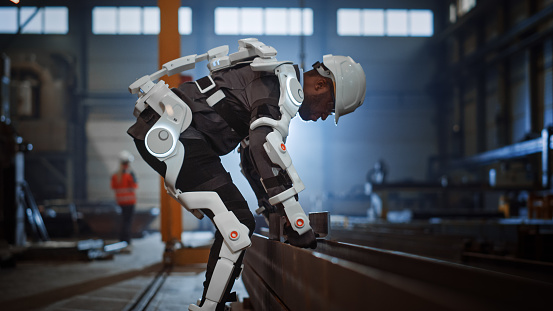 Black African American Engineer está probando un exoesqueleto biónico futurista y recogiendo objetos metálicos en una fábrica de la industria del acero pesado. El contratista es piezas de acero de elevación pesada en una carcasa alimentada. photo