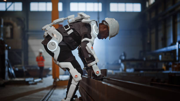 Black African American Engineer is Testing a Futuristic Bionic Exoskeleton and Picking Up Metal Objects in a Heavy Steel Industry Factory. Contractor is Heavy Lifting Steel Parts in a Powered Shell. black african american engineer está probando un exoesqueleto biónico futurista y recogiendo objetos metálicos en una fábrica de la industria del acero pesado. el contratista es piezas de acero de elevación pesada en una carcasa alimentada.