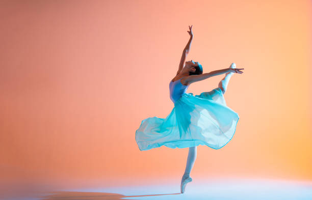 istock Ballerina in a light dress is dancing on colored background with backlight 1290246133