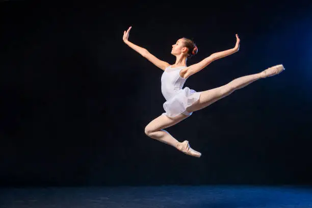 Ballerina in a white dress flying in a jump on a black background