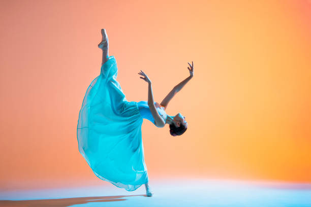 istock Ballerina in a light blue dress is dancing on colored backlit background 1290246164