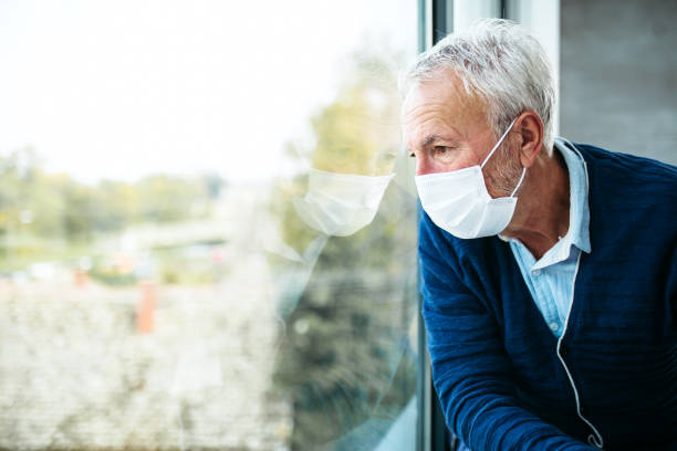 istock Senior adult in isolation looking through window with protective mask 1290247625