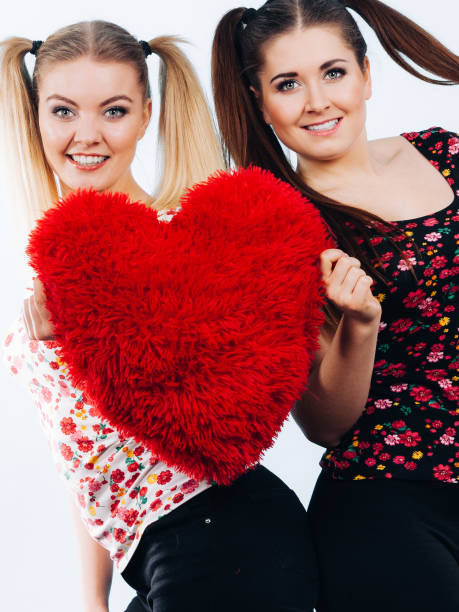 istock Happy two women holding heart shaped pillow 1290248604
