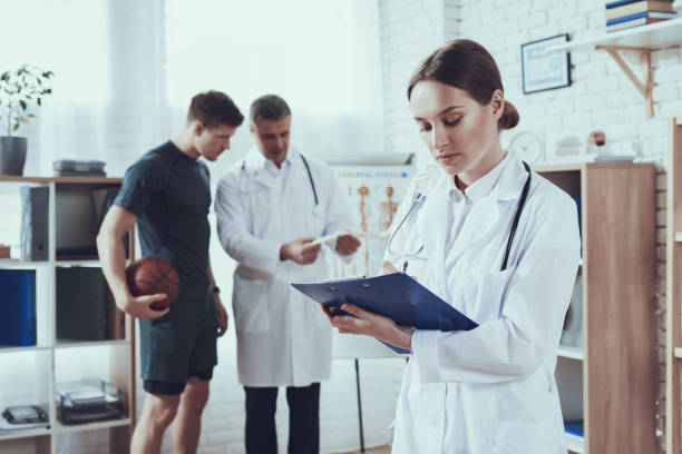 Male and female doctors with stethoscopes in office. Doctor is talking to basketball player. Male and female doctors in white gowns with stethoscopes in office. Doctor is talking to basketball player. professional sportsperson stock pictures, royalty-free photos & images