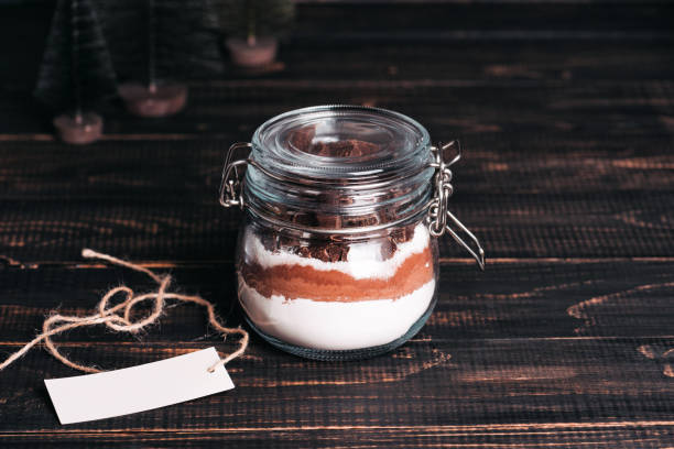 Christmas gift cookie mix in glass jar on dark wooden table Christmas gift cookie mix in glass jar on dark wooden table. Layers of flour, cocoa powder, sugar. Ingredients for ginger bread. Copy space for your text cake jar stock pictures, royalty-free photos & images