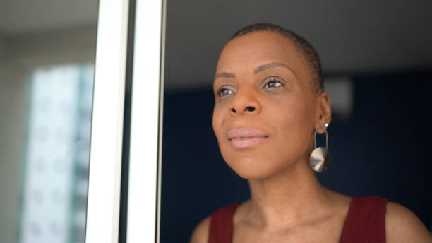 istock Mature woman looking through window at her house 1290258604