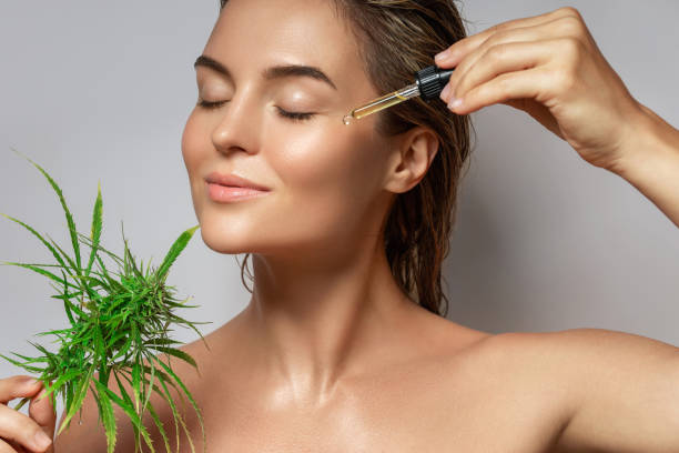 CBD cosmetics concept. Beautiful woman with a cannabis leaf CBD cosmetics concept. Beautiful woman with a cannabis leaf on gray background face serum stock pictures, royalty-free photos & images