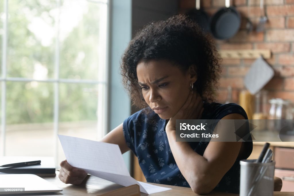Frustrated young african american woman reading letter with bad news. Frustrated young african american woman reading paper letter with bad news, stressed of getting bank debt or loan rejection notification, feeling confused of termination notice, sitting at table. Healthcare And Medicine Stock Photo