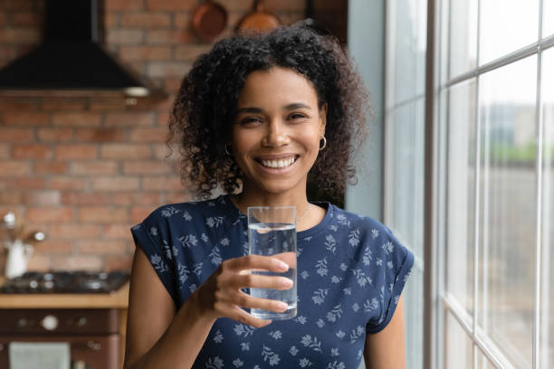 gelukkige jonge multiraciale etnische vrouw die glas water houdt. - drinking water stockfoto's en -beelden