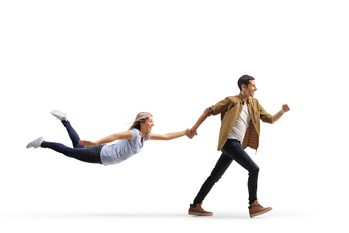 Full length profile shot of a casual man running and holding a woman with his hand isolated on white background