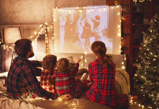 family mother father and children watching projector, film, movi happy family in checkered pajamas: mother father and children watching projector, film, movies with popcorn in christmas holiday evening   at home film industry stock pictures, royalty-free photos & images