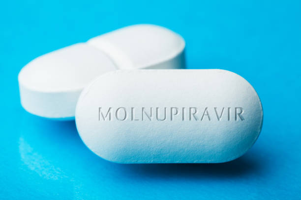 COVID-19 experimental antiviral drug MOLNUPIRAVIR COVID-19 experimental antiviral drug MOLNUPIRAVIR, two white pills with letters engraved on side, potential experimental WHO Coronavirus cure, pandemic outbreak crisis, isolated on blue background historical geopolitical location photos stock pictures, royalty-free photos & images