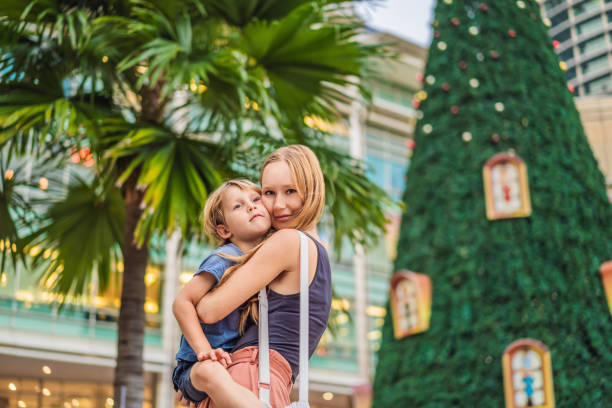 maman et fils sur l’arrière-plan de l’arbre de noël et des palmiers décorés dans l’endroit tropical de vacances - christmas palm tree island christmas lights photos et images de collection