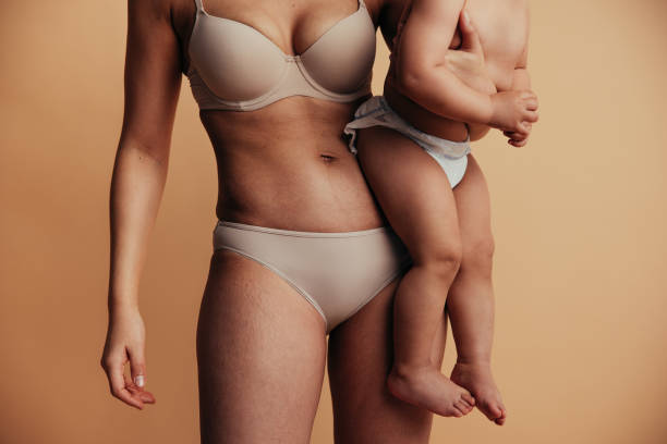 Postpartum mom close up Cropped shot of mother carrying her baby. Female holding her baby in her arm against brown background. pregnancy body stock pictures, royalty-free photos & images